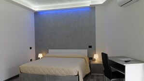 A modern bedroom with a bed, bedside tables, a desk, and a chair. - Albergo 3 Torri (Maddaloni)