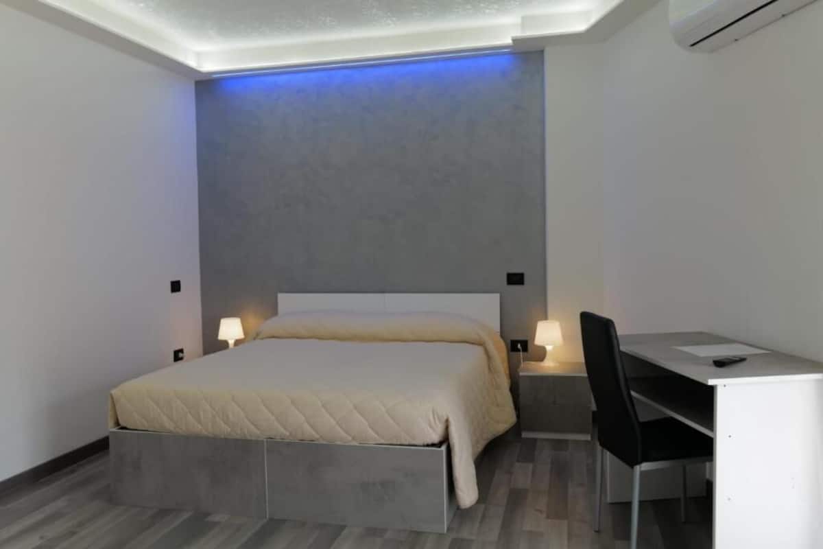 A modern bedroom with a bed, bedside tables, a desk, and a chair.