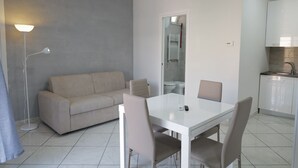 A modern living room with a sofa, a dining table with chairs, a floor lamp, and a kitchen area with cabinets and a sink. - Albergo 3 Torri (Maddaloni)