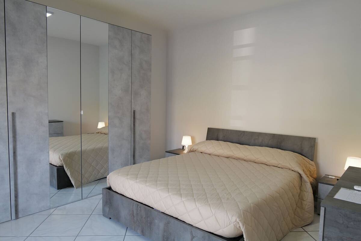 A bedroom with a bed, bedside tables, a mirror, and a wardrobe.