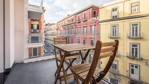 A balcony with a wooden table and chairs, overlooking a street with colorful buildings.