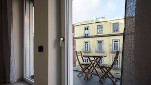 A balcony with a table and chairs, a view of a yellow building, and a door leading to an interior space.