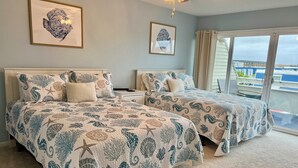 Une chambre avec deux lits, chacun agrémenté d’une couvre-lit sur le thème de la mer, d’une table de chevet et d’une grande fenêtre donnant sur la mer.