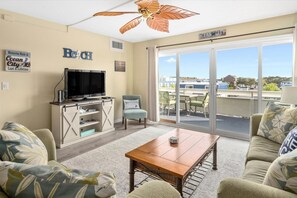 Uma sala de estar com televisão, mesa de centro e sofá. Há uma placa na parede que diz 'Ocean City'.