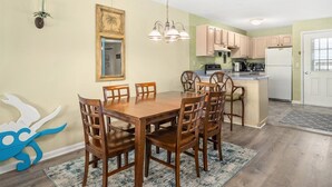 Un coin repas avec une table et des chaises en bois, un luminaire suspendu et une cuisine en arrière-plan.
