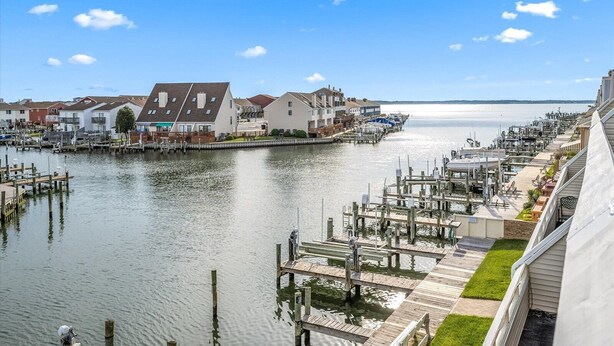 Un port de plaisance avec des bateaux amarrés, une rangée de maisons et un ciel dégagé.