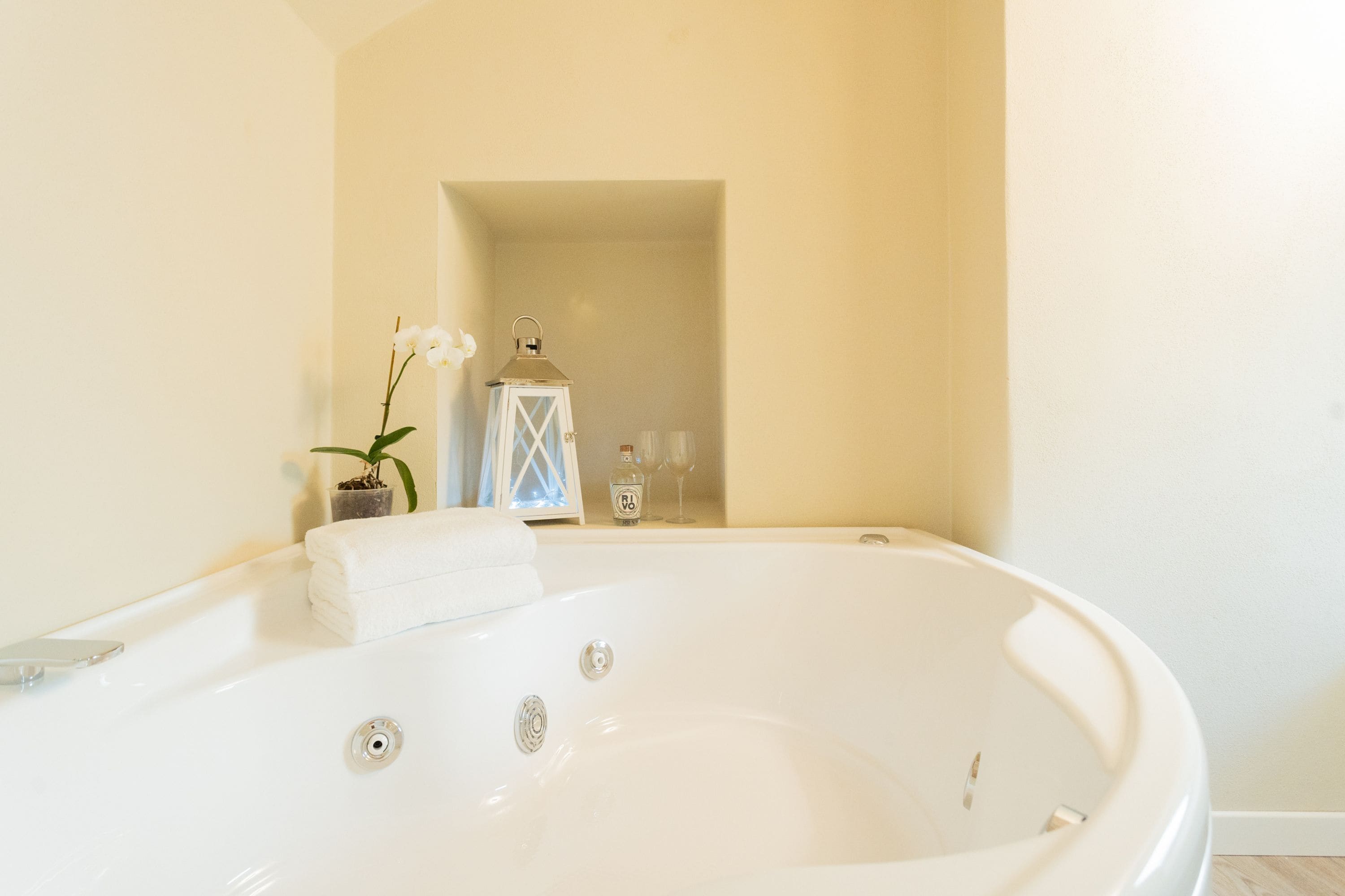 Un baño moderno con una bañera grande, una orquídea en maceta, un farol y un vaso de agua en la encimera.