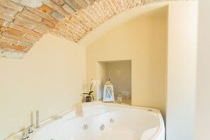 Ein Badezimmer mit einer großen Badewanne, einer kleinen Topforchidee, einer weißen Laterne und einer Parfumflasche.