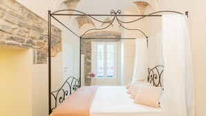 A four-poster bed with a canopy, a stone wall, and a window with a view of the street. - Romantic Escape in the 400s (Como)