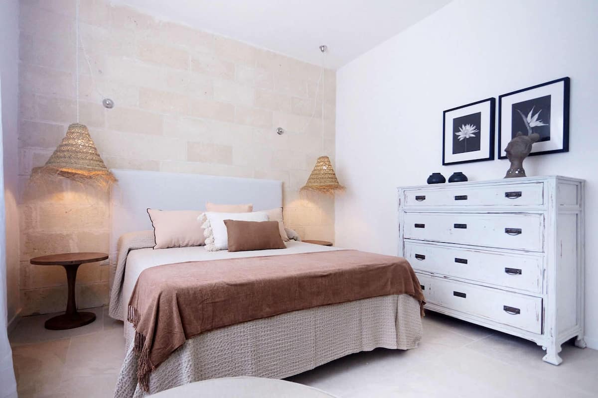 A bedroom with a bed, bedside lamps, a dresser, and two framed pictures on the wall.