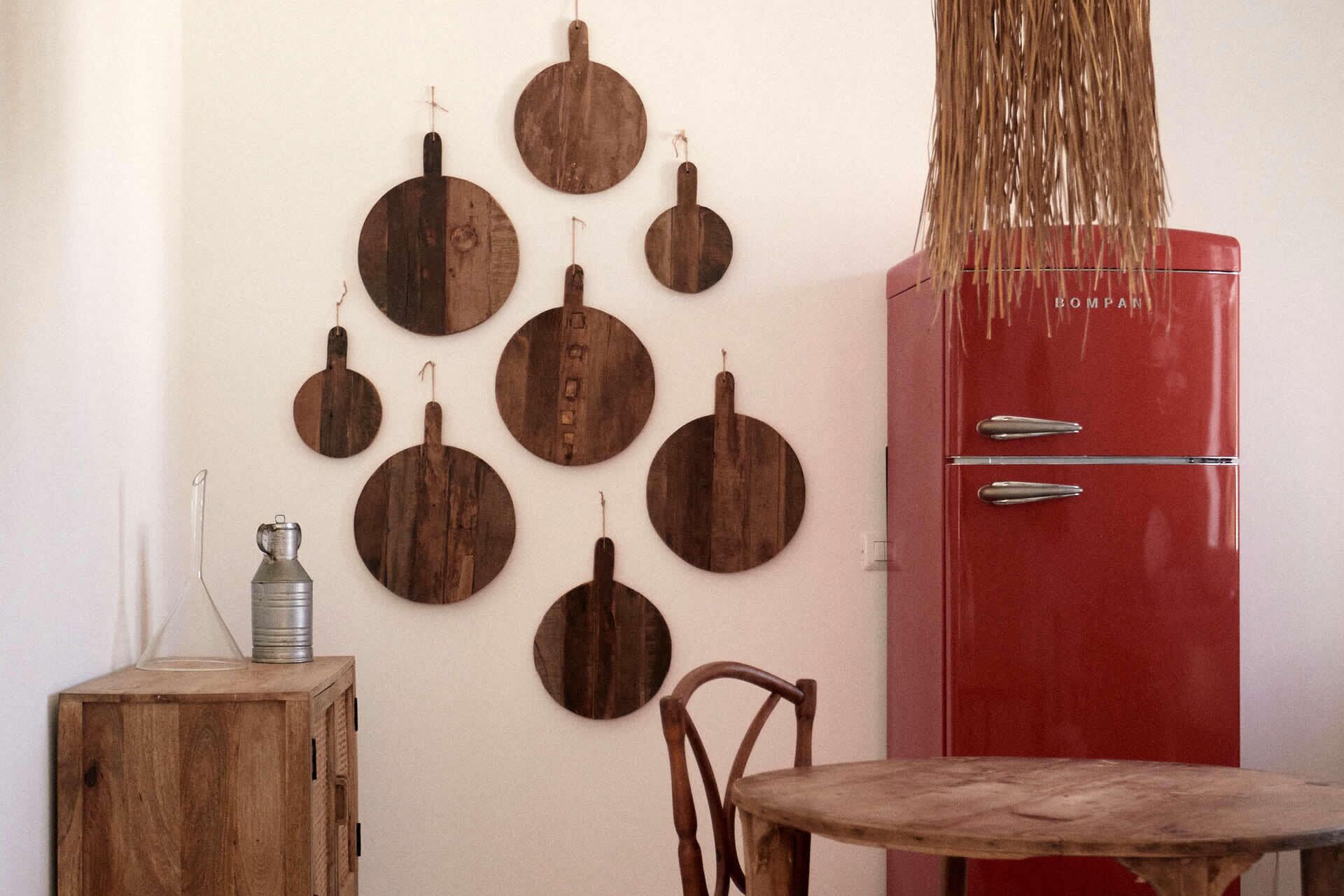 Una habitación con un refrigerador antiguo rojo, adornos de madera montados en la pared, un armario de madera y una silla rústica.