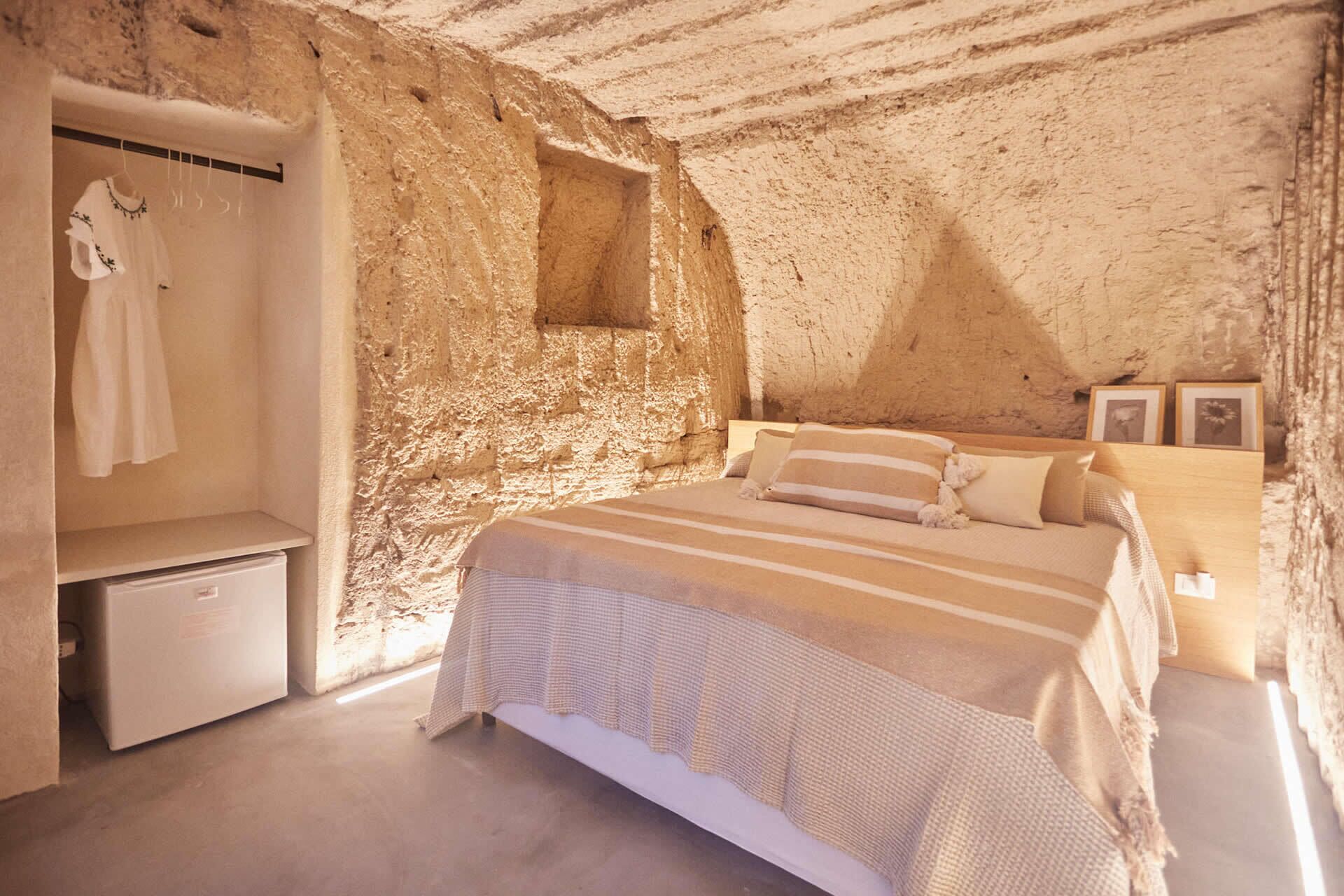 A bedroom with a stone wall, a bed with striped bedding, a bedside table, and a hanging garment rack.