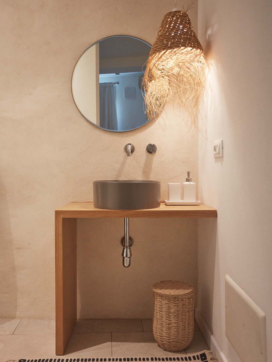 Un baño con un espejo redondo, un lavabo circular, un perchero y una lámpara colgante.