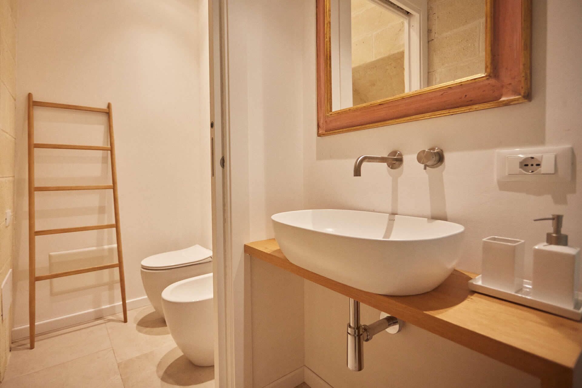 Une salle de bain avec un lavabo blanc, un meuble-lavabo en bois, un miroir avec un cadre doré et des toilettes.