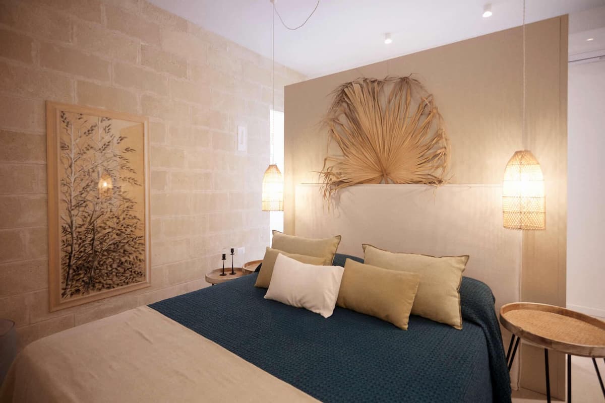 A modern bedroom with a large bed, a wall-mounted artwork, and two wall sconces.