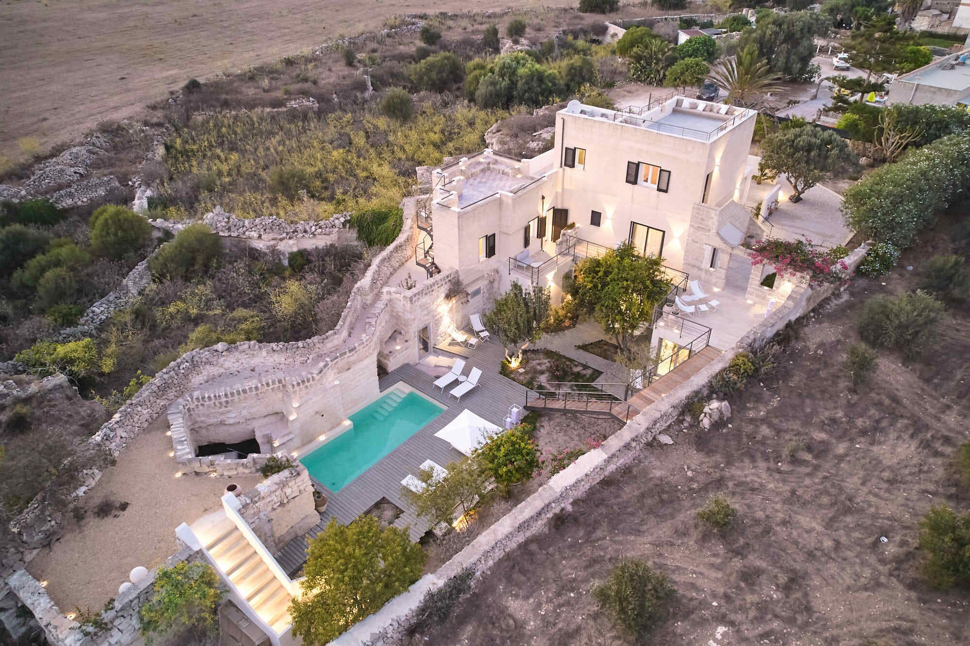 Una villa moderna con piscina, mobiliario exterior y un muro de contención de piedra.