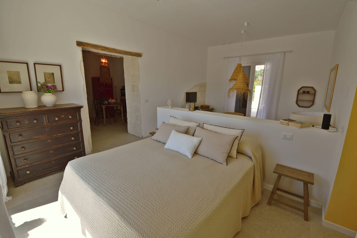A bedroom with a large bed, a dresser, a mirror, and a small stool.