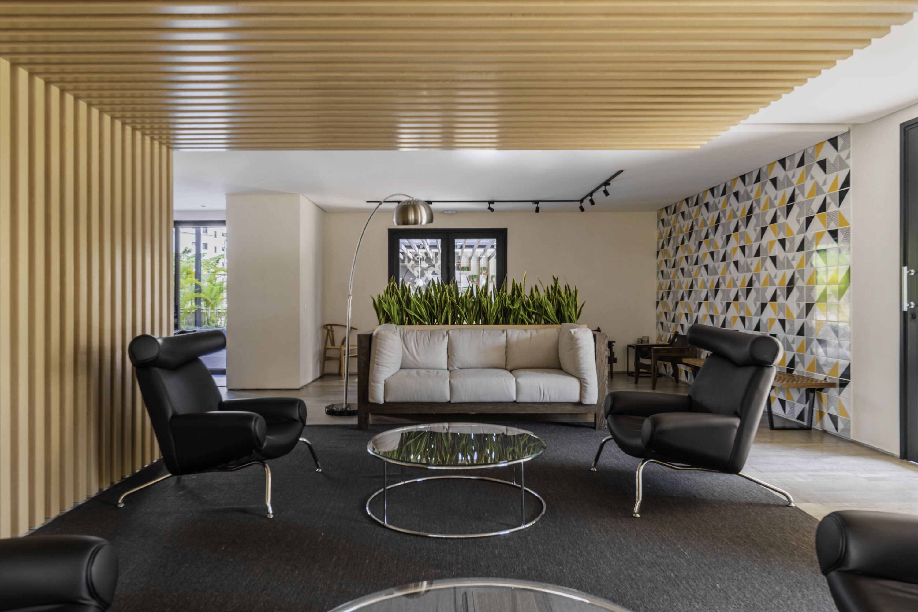 A modern living room with a sofa, two armchairs, and a glass coffee table.