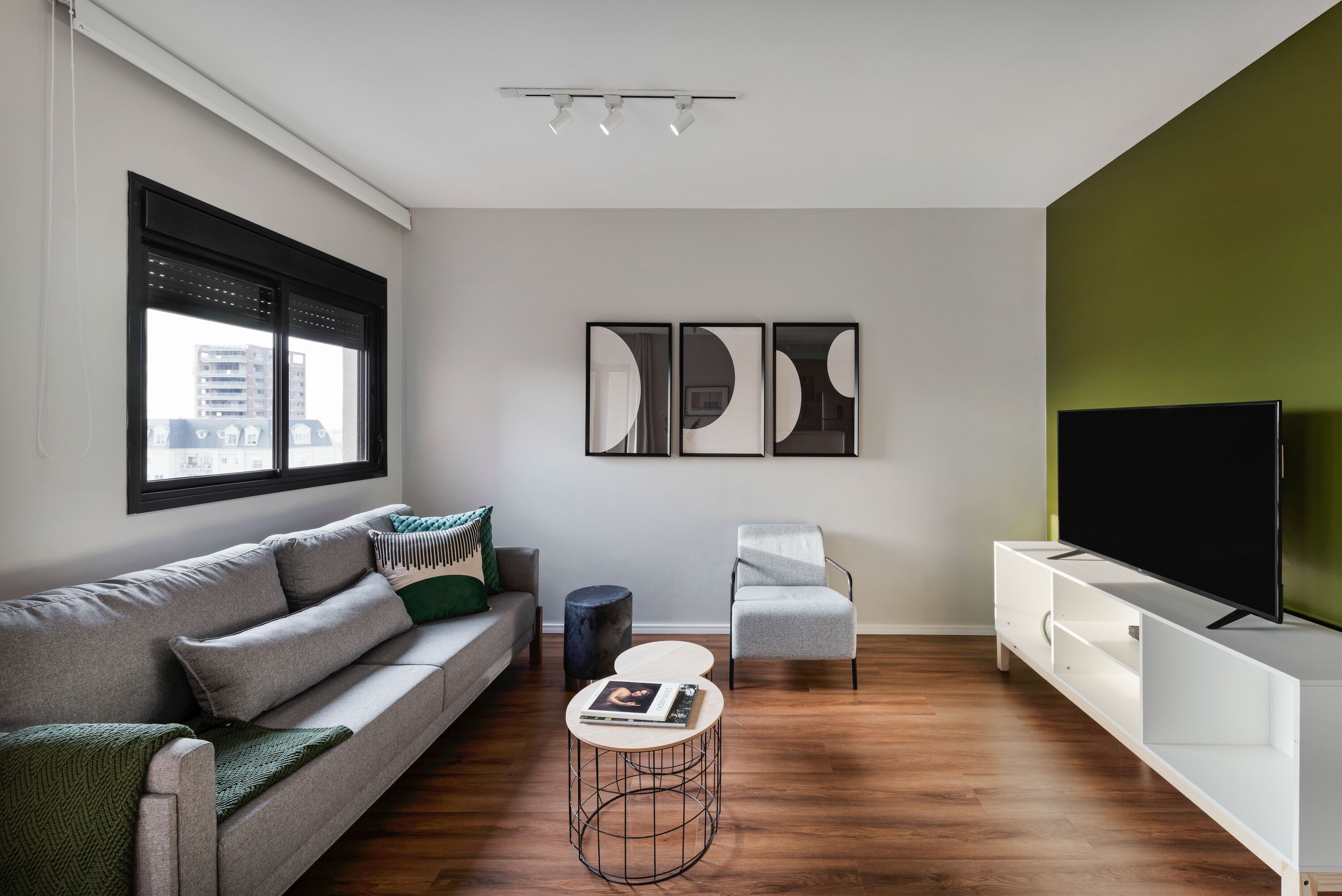 A modern living room with a grey sofa, a white armchair, a coffee table, and a TV on a white stand.