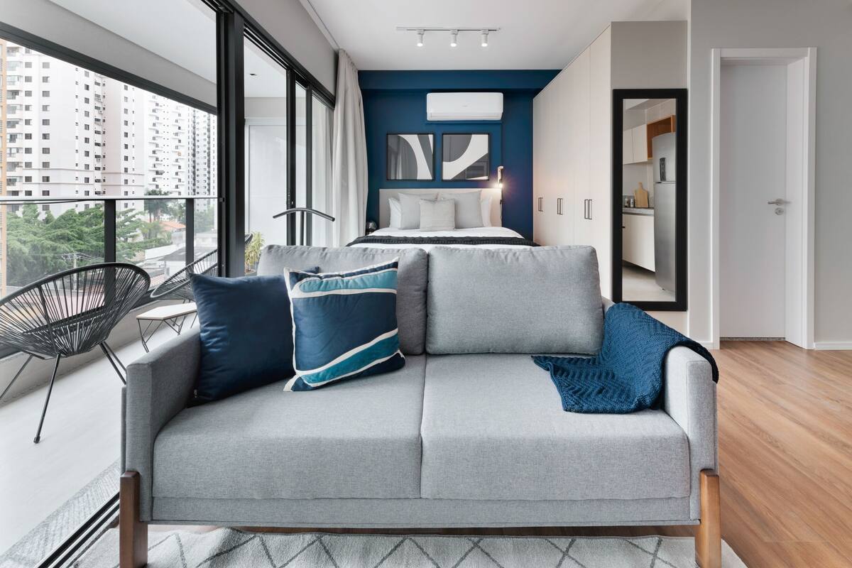 A modern living room with a grey sofa, a black chair, and a view of the cityscape through large windows.