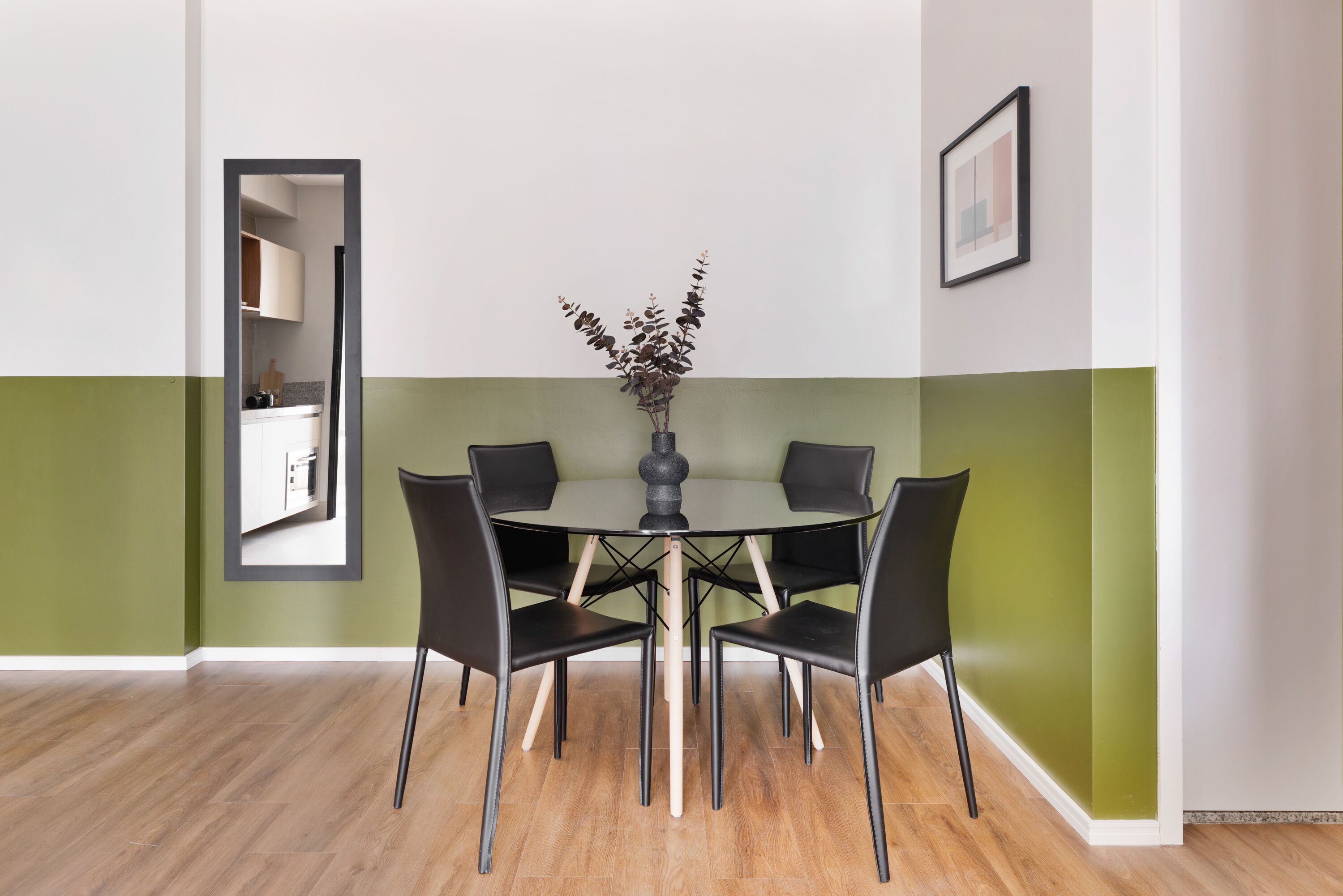 A dining area with a round table, four chairs, and a vase with branches.