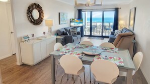 Uma sala de estar moderna com área de jantar, televisão e varanda vista para o mar.