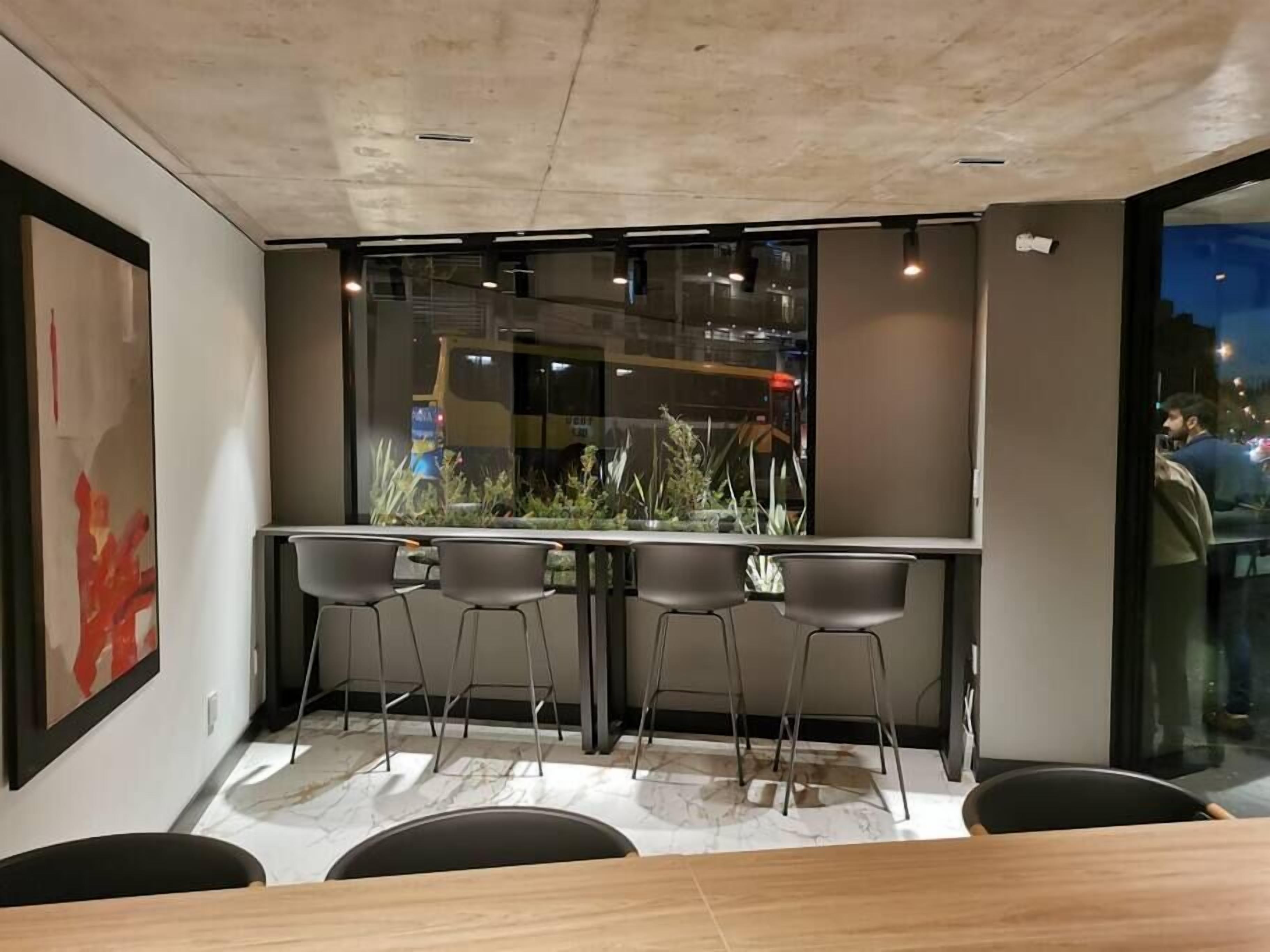 A modern dining area with a long table, four chairs, and a window with a view of the city at night.