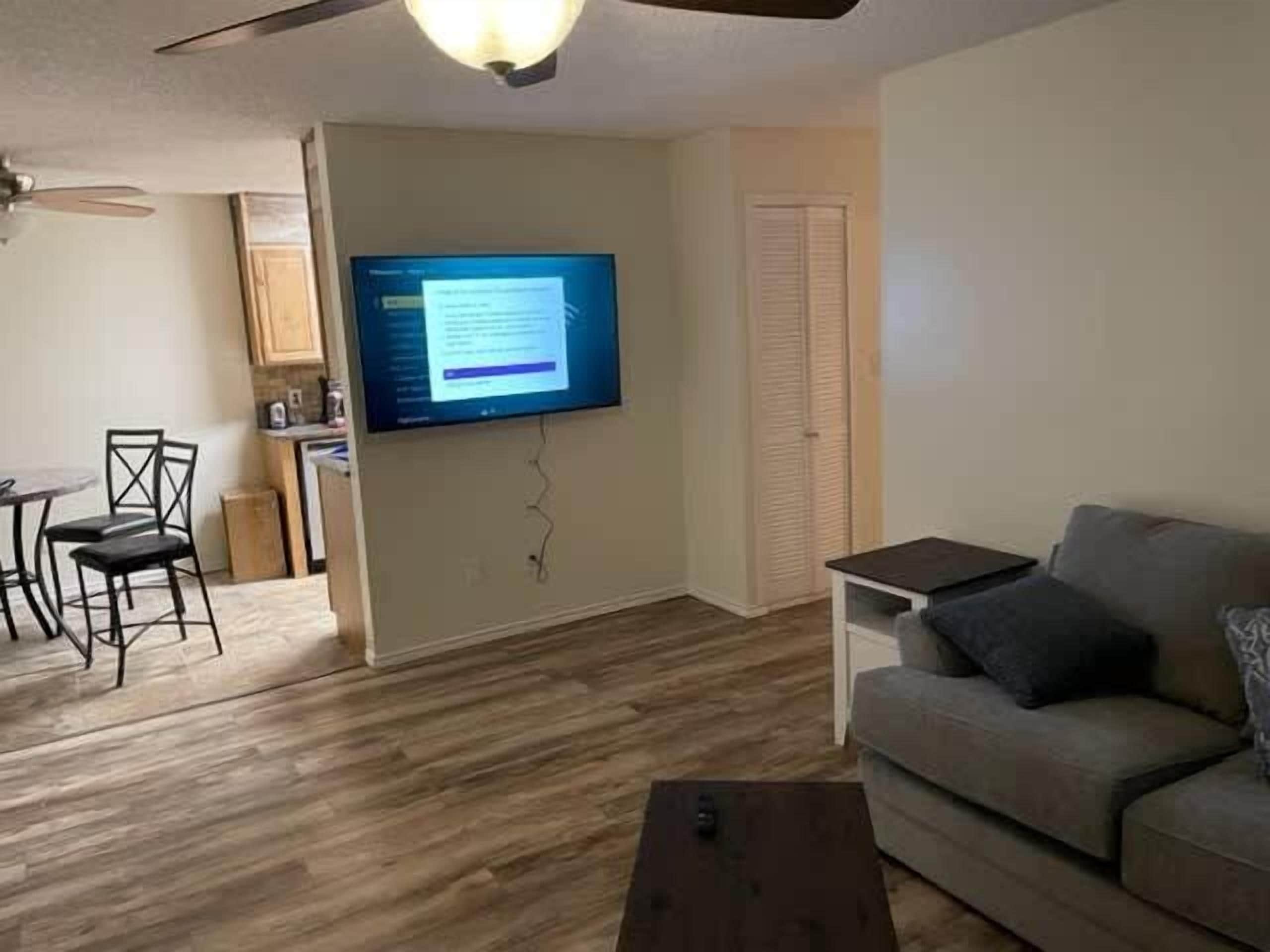 Un salon doté d’un téléviseur à écran plat fixé au mur, d’un canapé, d’une table basse et d’un coin repas avec des chaises.