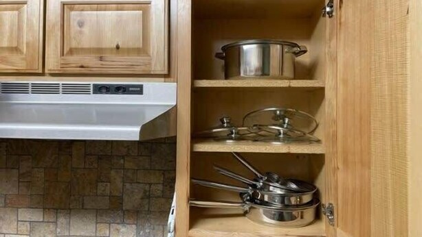 Une cuisine avec des meubles de rangement en bois, une hotte de cuisine en acier inoxydable et divers ustensiles de cuisine et casseroles disposés sur des étagères ouvertes.