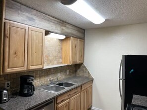 A kitchen with wooden cabinets, a granite countertop, a double sink, and a black refrigerator. - Comfortable downstairs 2 bed next to Fort Sill! (Lawton)