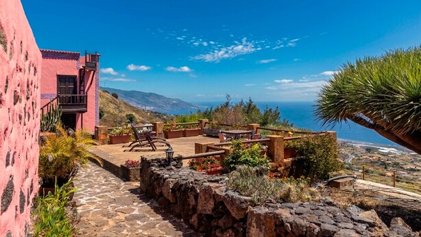 A pink building with a patio area featuring outdoor furniture and plants, overlooking a coastal landscape. - Casa Celeste, swimming pool with panoramic views in the east of La Palma (Villa de Mazo)