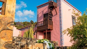 A pink building with a balcony, a stone wall, and cacti. - Casa Celeste, swimming pool with panoramic views in the east of La Palma (Villa de Mazo)