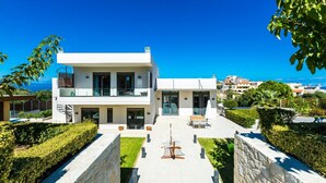 A modern two-story house with a balcony, a patio with outdoor furniture, and a view of the sea. - Lux Villa 600mt to beach★Gym & Basketball ★Heated pool★100 mt to Taverna (Platanias)