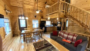 Een houten chalet van binnen met een eethoek, een bank en een trap.