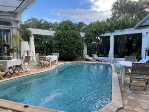 A pool area with lounge chairs, a table, and a pergola.