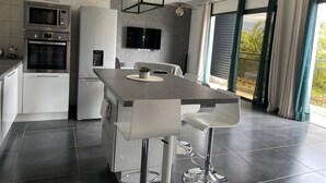 A modern kitchen with built-in appliances, a dining area with bar stools, and large windows with curtains.