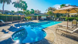 A swimming pool with lounge chairs and umbrellas, surrounded by palm trees and houses.