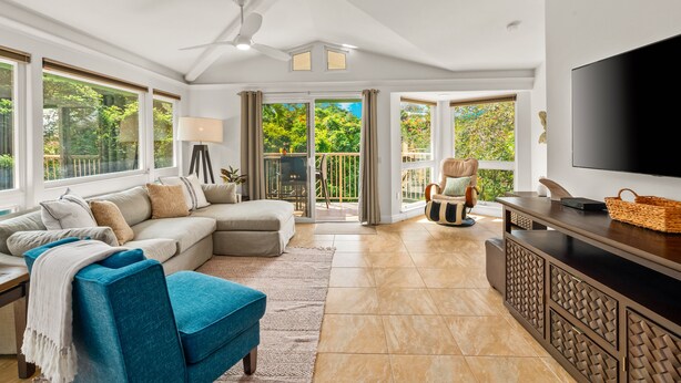 A spacious living room with a sectional sofa, a blue armchair, a TV, and a balcony with glass doors.