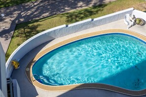 Une piscine à bord incurvé, un petit espace aménagé et une plante en pot.