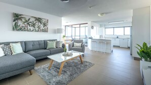 Una sala de estar moderna con un sofá gris, una mesa de centro y una zona de cocina al fondo.