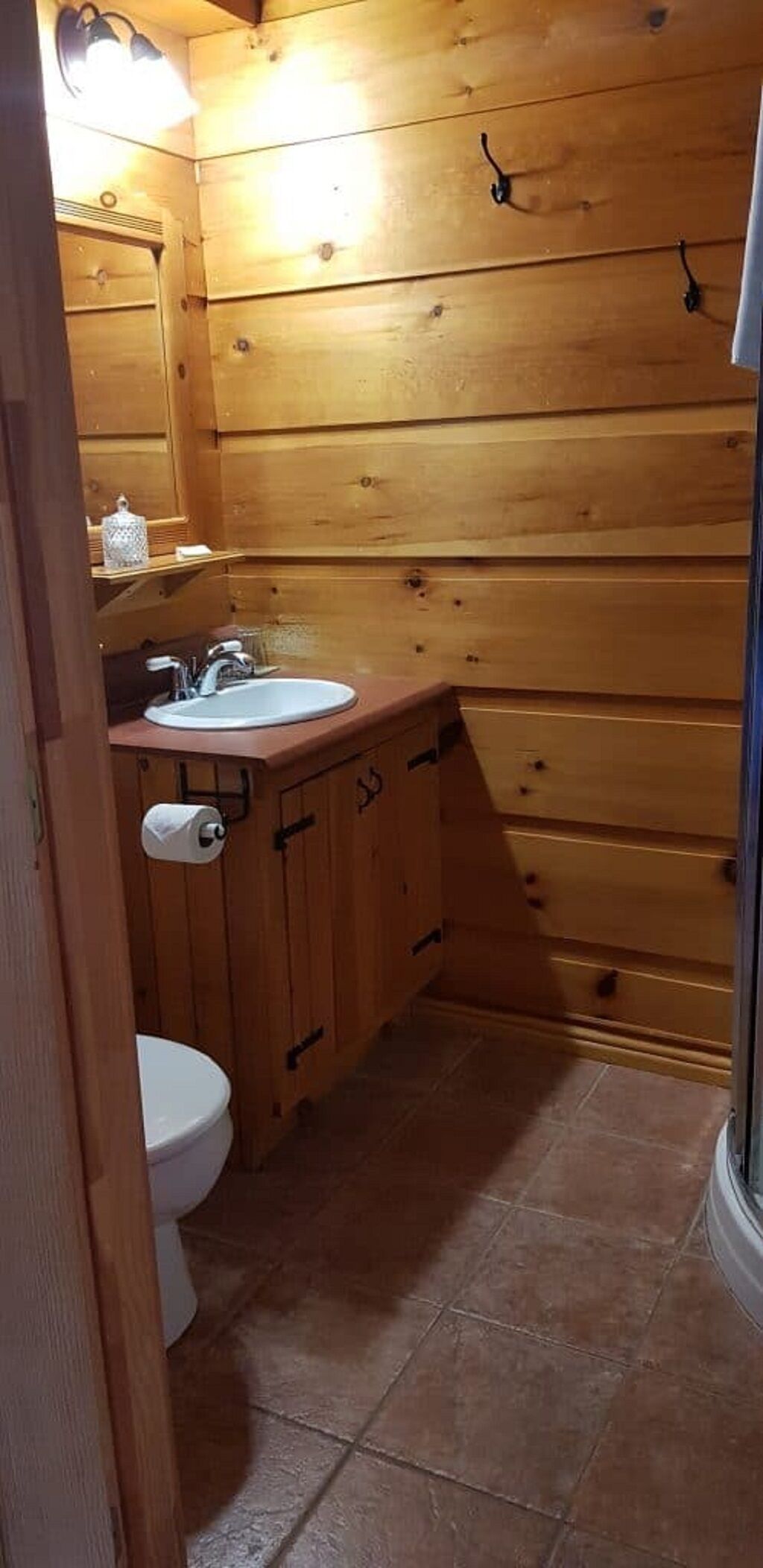 A wooden cabin-style bathroom with a sink, toilet, and a towel rack.