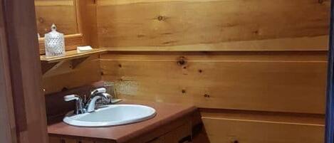 A wooden cabin-style bathroom with a sink, toilet, and a towel rack.
