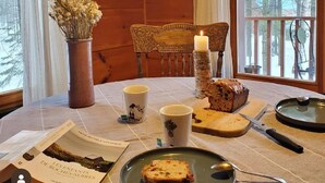 Interior de una cabaña de madera con una mesa lista para dos personas, con una vela, un pan y un plato con una rebanada.