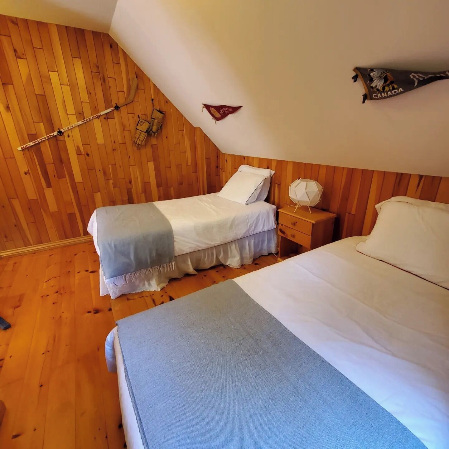 Een slaapkamer met twee bedden, houten wanden en een schuin dak.