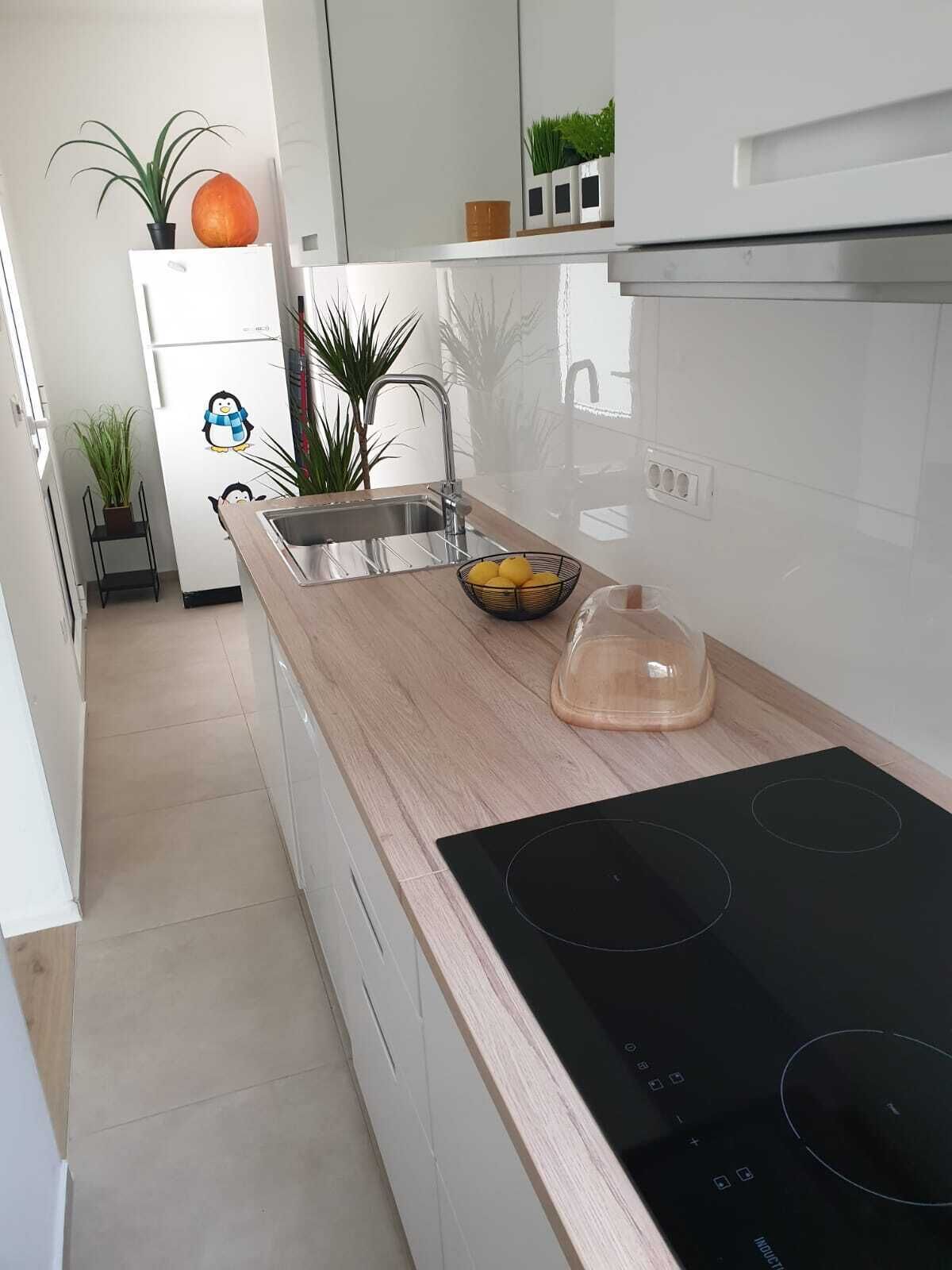 A modern kitchen with a black induction cooktop, a stainless steel sink, and a wooden countertop.