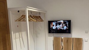 Una habitación con un armario blanco, un banco de madera y un televisor en la pared.