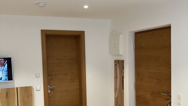 Habitación de hotel con suelo de madera, una cama, un banco, dos puertas y un televisor en la pared.