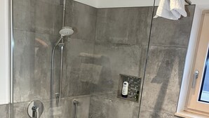 Un box de ducha moderno con puerta de vidrio, un cabezal de ducha manual y un accesorio de ducha de mano.