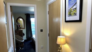 A hotel hallway with a wooden door, a lamp, a small table with a bowl, and a poster on the wall. - Luxury Ouseburn flat with city & river views (Tyne and Wear)