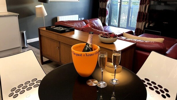A modern room with a wooden table, a bottle of champagne, and two glasses. - Luxury Ouseburn flat with city & river views (Tyne and Wear)